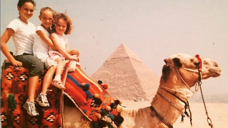 children riding a camel in front of an Egyptian pyramid